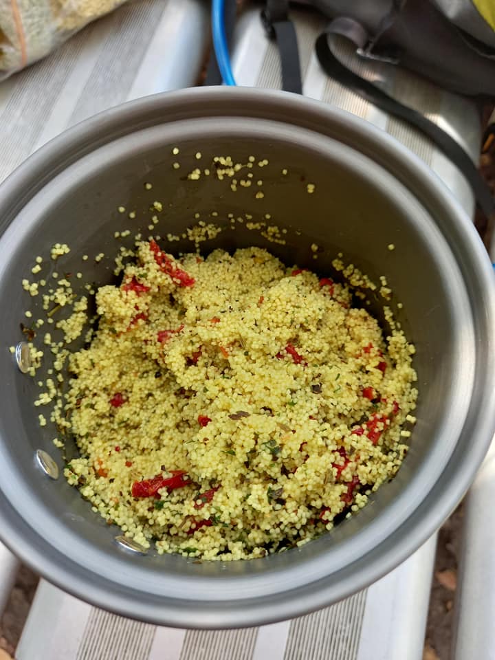Image of a small pot containing a mixture of couscous, finely sliced herbs and sundried tomatoes.